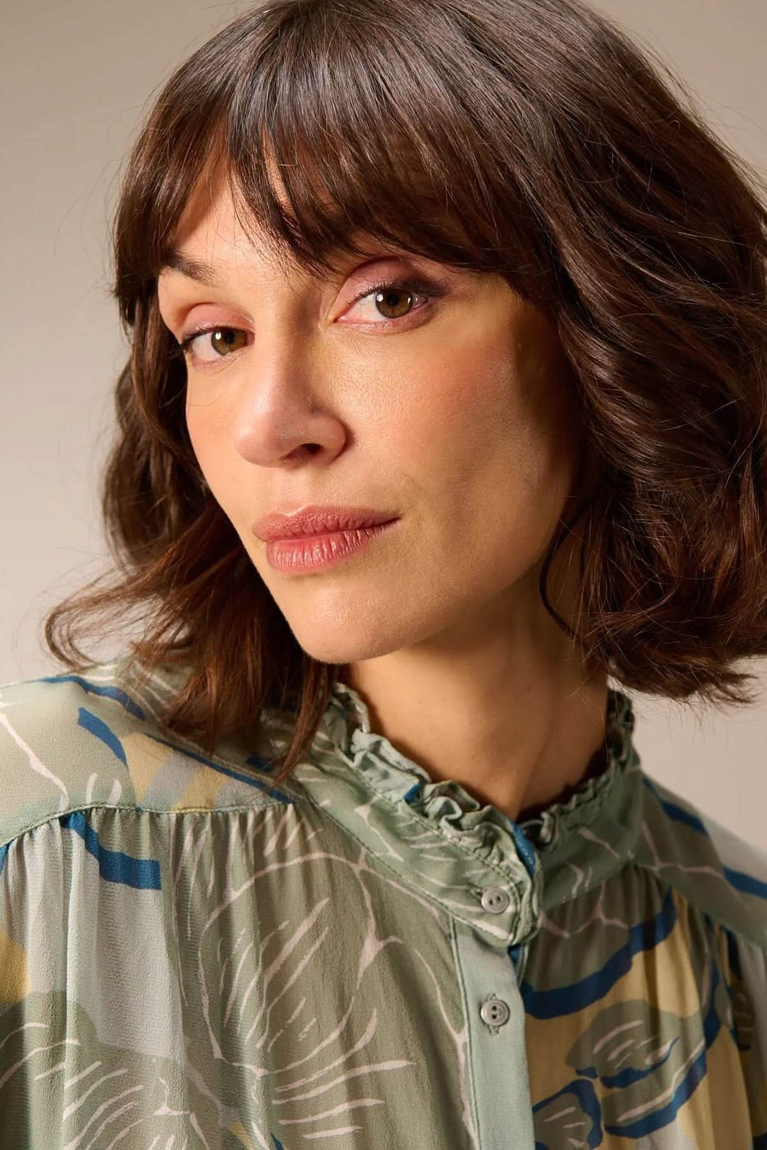 Femme portant une blouse fluide à manches longues avec col montant et finition froncée, silhouette légère et féminine adaptée pour la mi-saison.