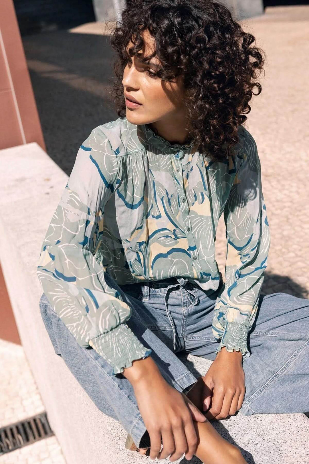 Femme portant une blouse fluide à manches longues avec motif floral élégant, col montant froncé et poignets smockés, pour mi-saison.