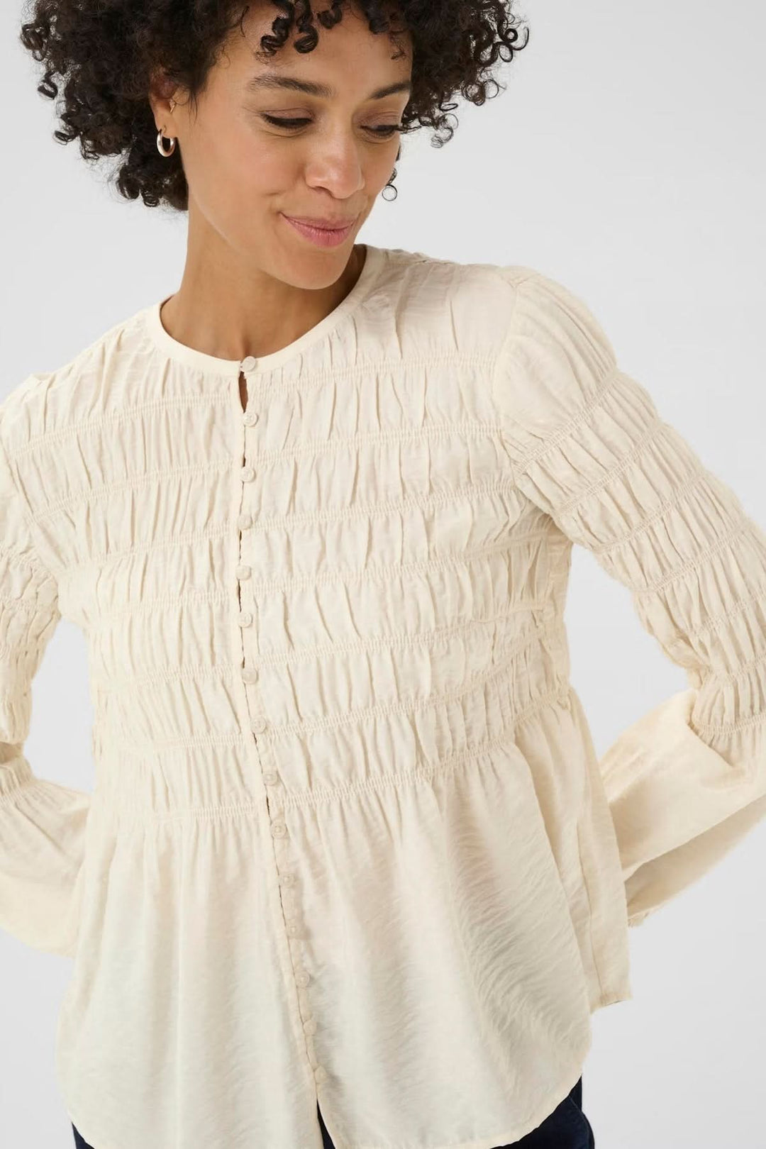 Femme portant une blouse à fronces avec encolure ronde et patte boutonnée, style romantique et féminin, idéal pour un look casual chic.
