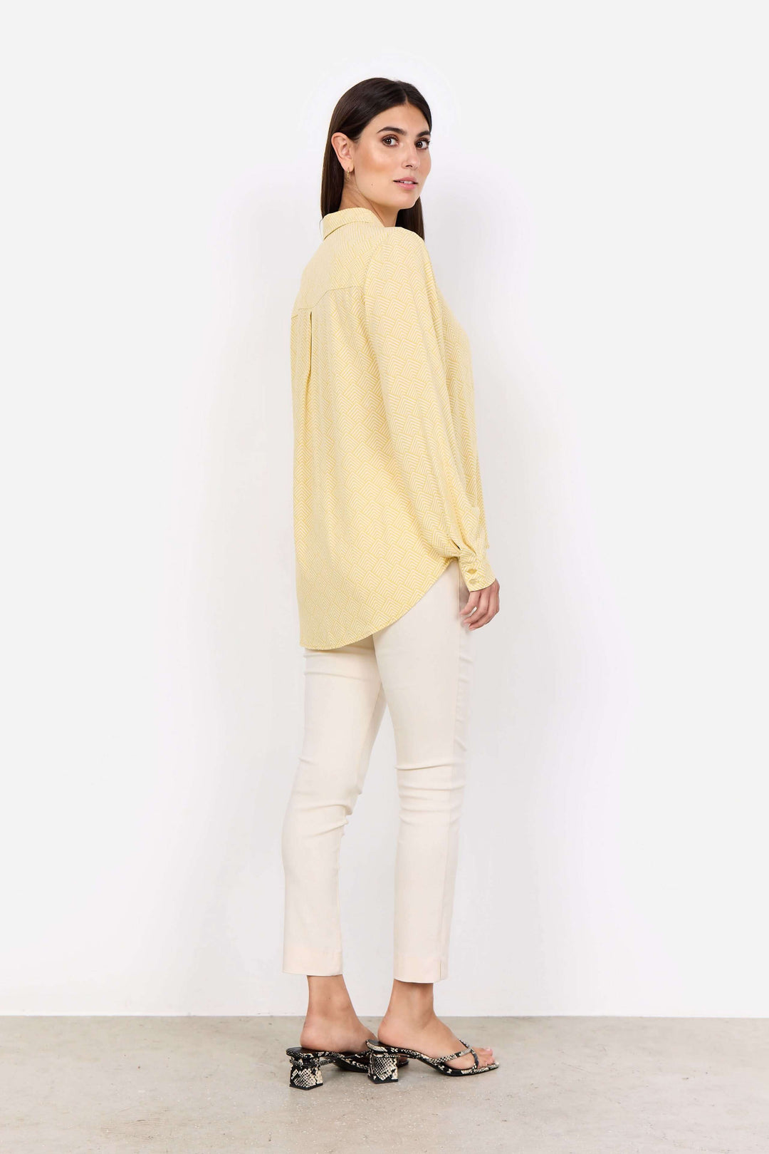 Blouse imprimée jaune avec col classique, vue de dos, portée avec un pantalon ajusté et des sandales.