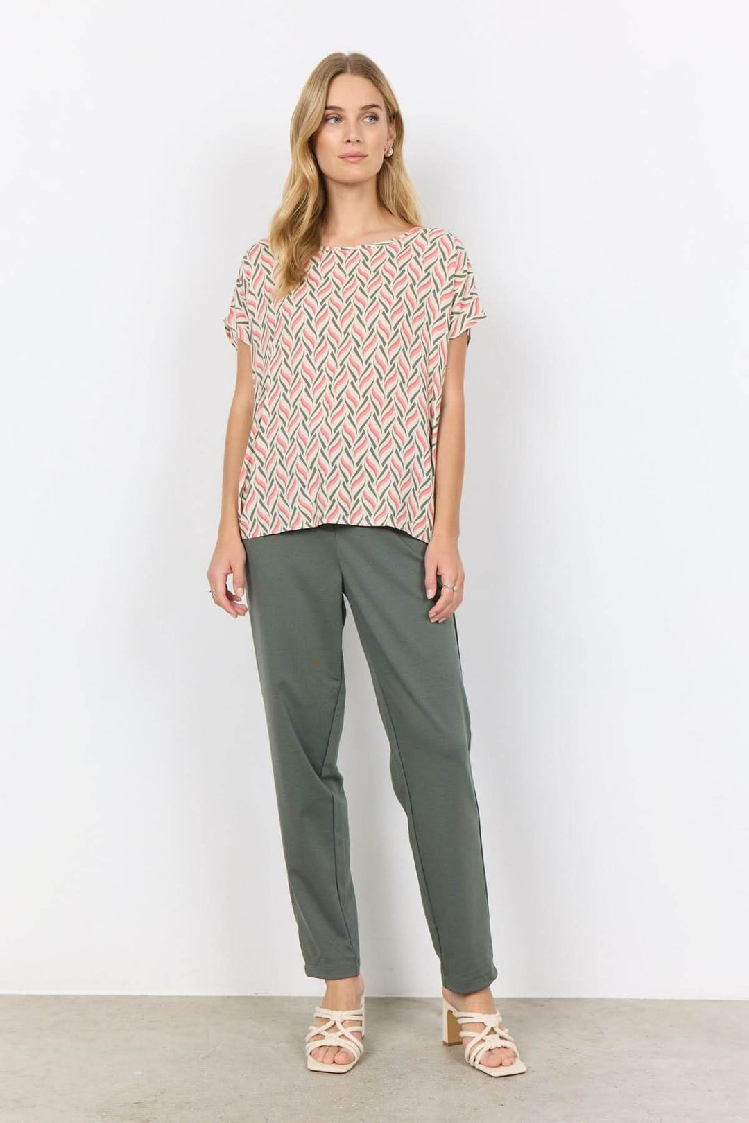 Femme portant une blouse imprimée abstrait en viscose Ecovero avec un pantalon élégant et des sandales.