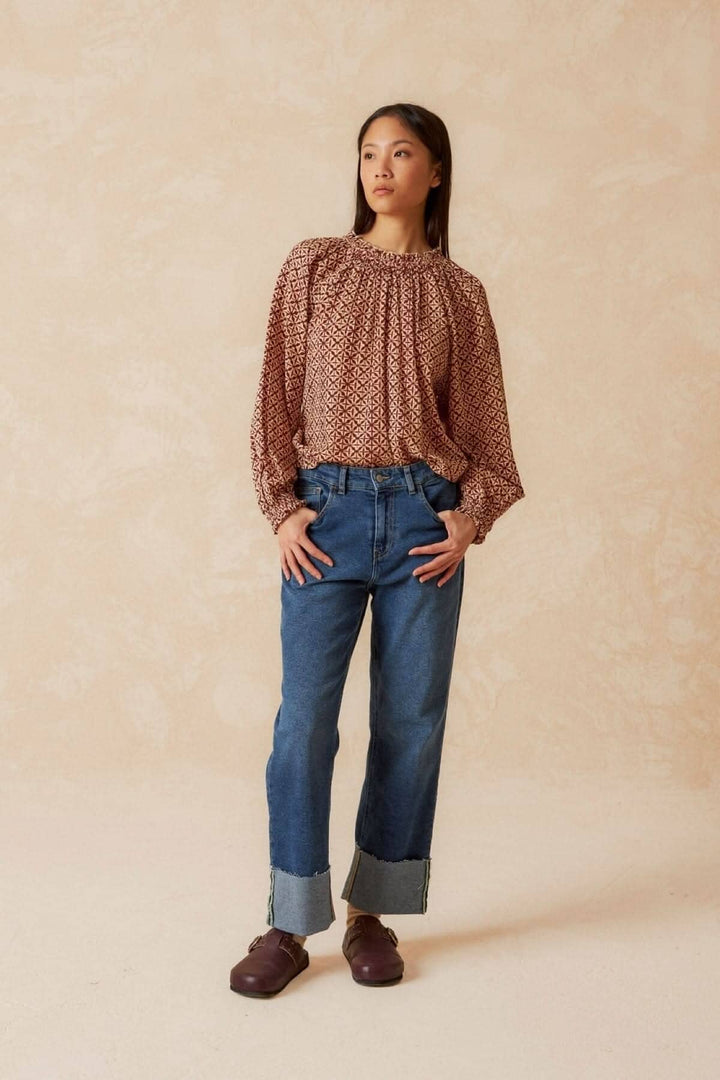 Femme portant une blouse imprimée mosaïque, manches longues, associée à un jean bleu, look moderne et chic.