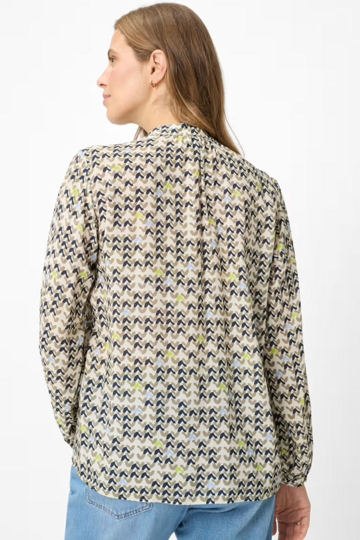 Femme portant une blouse imprimée à motif géométrique, vue de dos, en tissu léger et coupe droite assurant une silhouette féminine et fluide.
