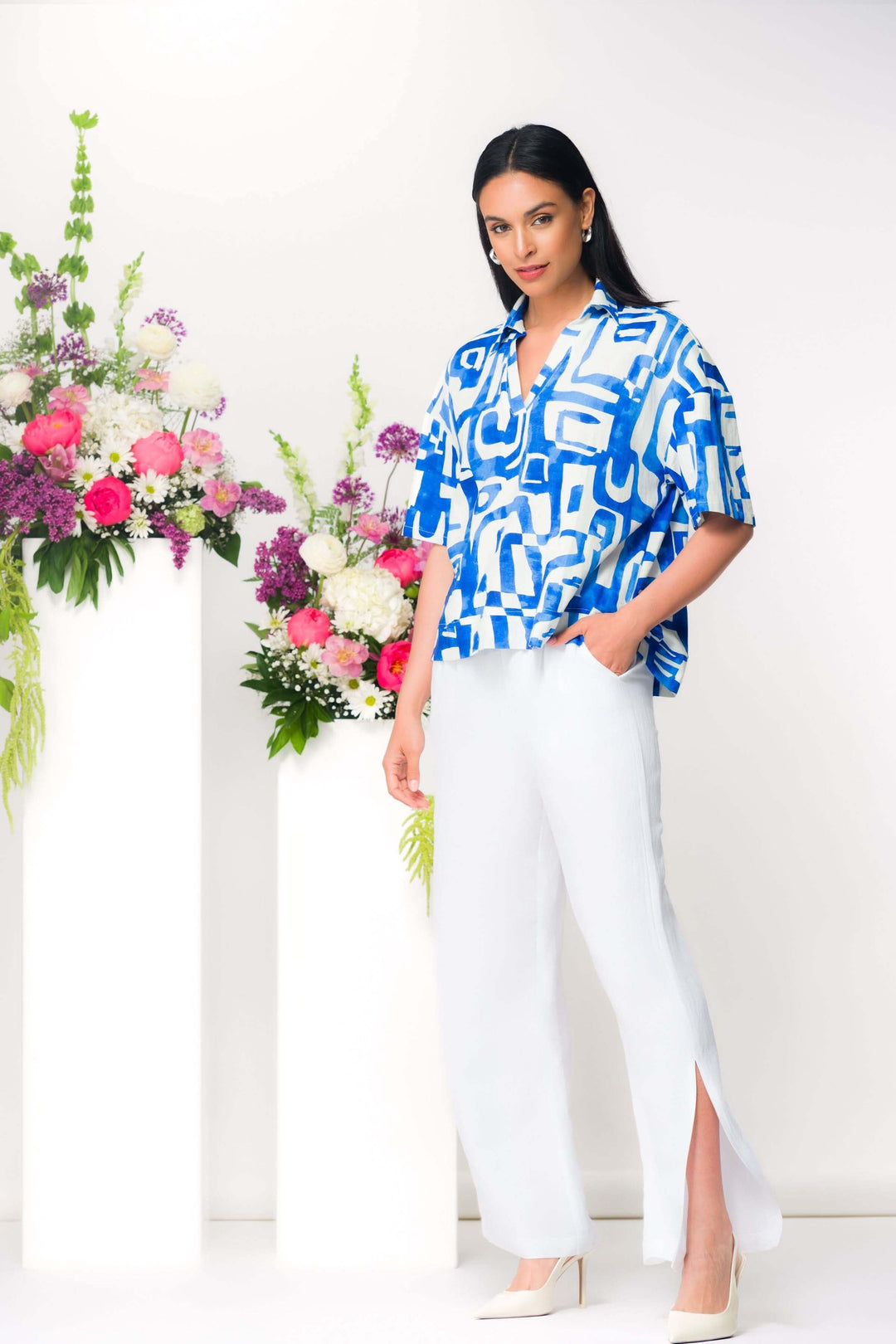 Blouse imprimée à coupe ample et col ouvert, avec imprimé graphique audacieux, portée par une femme devant des fleurs colorées.