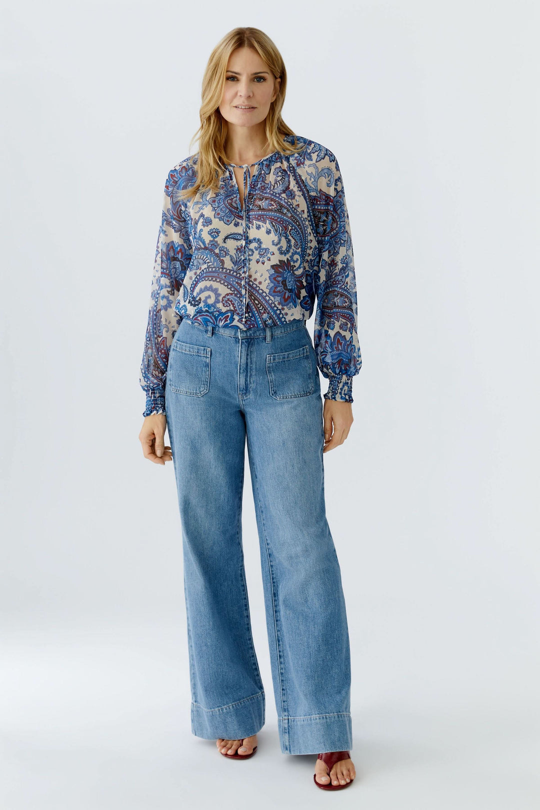 Femme portant une blouse imprimée à manches longues avec motif cachemire et jean, ajoutant une touche bohème et féminine à sa tenue.