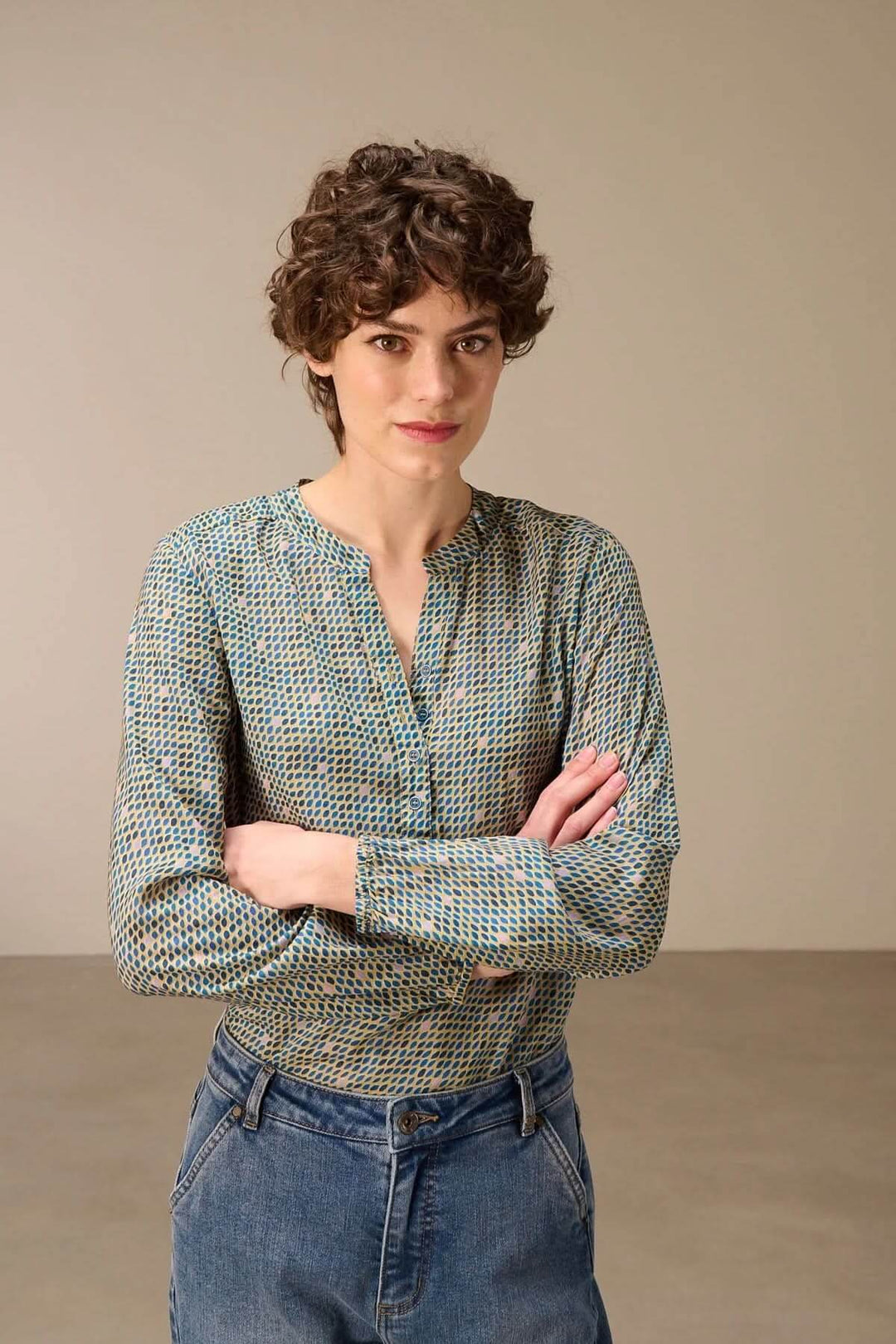 Femme portant une blouse imprimée à manches longues avec encolure fendue et motif graphique subtil, associée à un jean pour un style moderne.