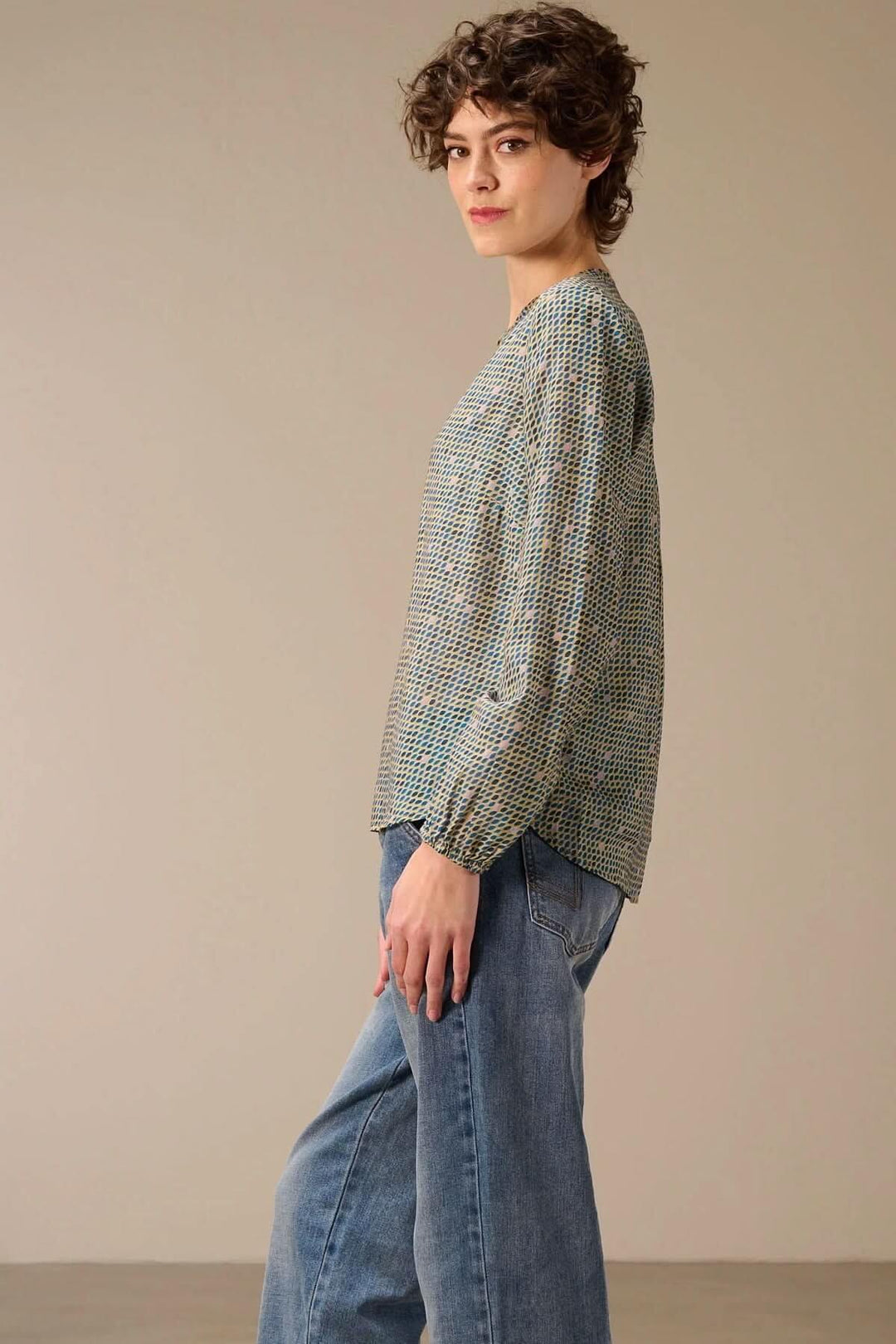 Femme portant une blouse imprimée à manches longues avec un jean, vue de profil élégante et décontractée.