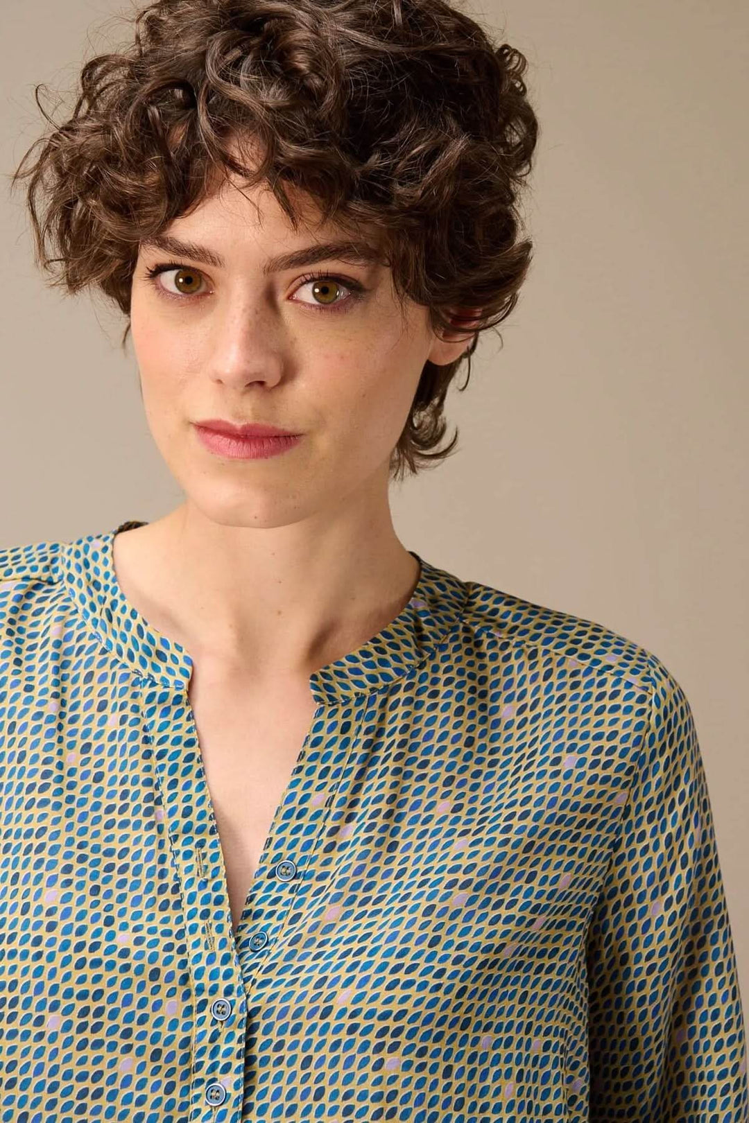 Blouse imprimée à manches longues avec encolure fendue, portée par un modèle, détail d'un motif graphique subtil.