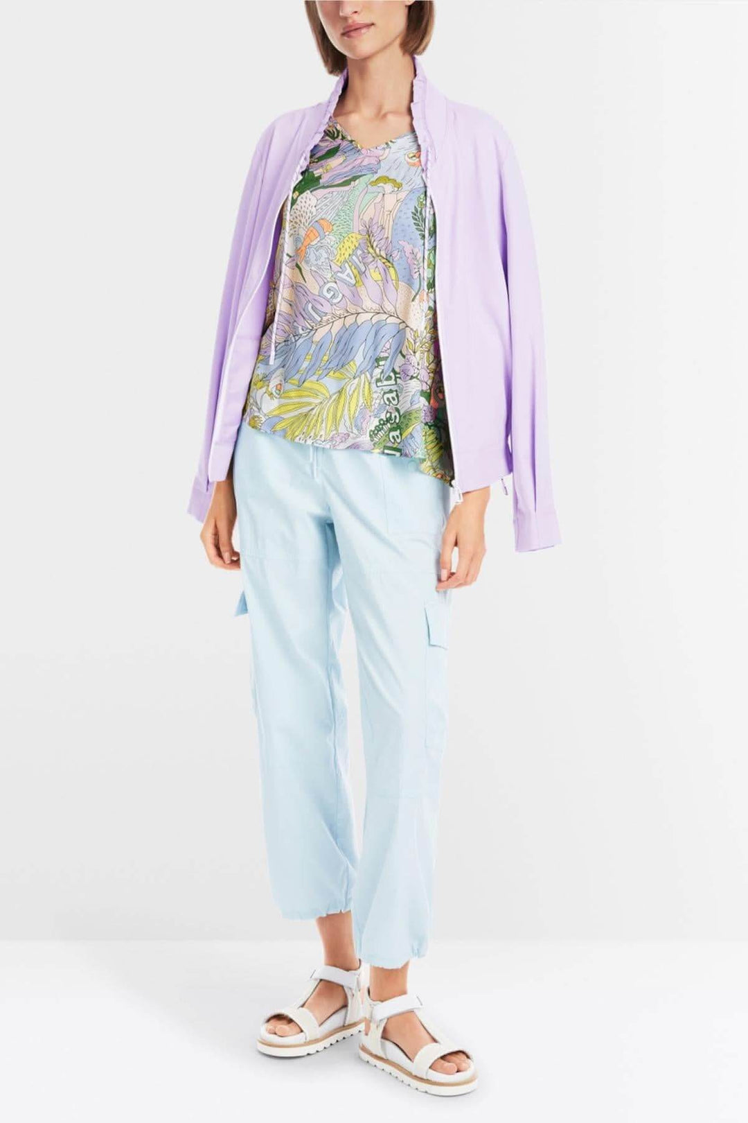 Femme portant une blouse imprimée sushi colorée avec un gilet lilas et un pantalon bleu clair.
