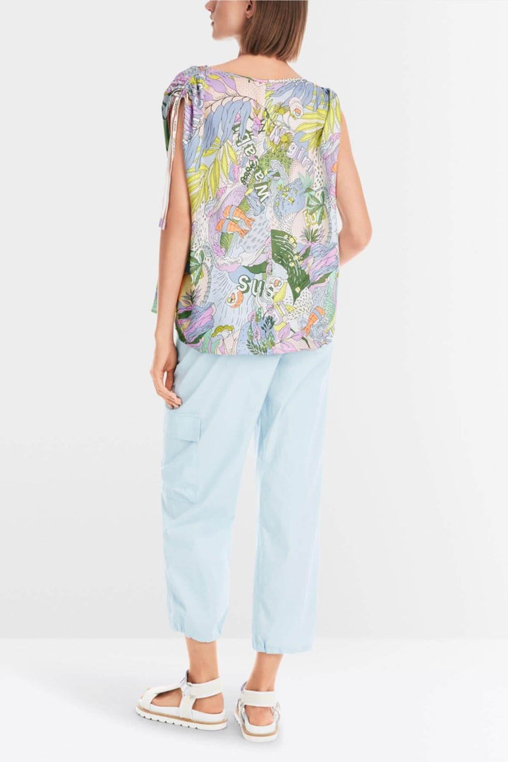 Blouse imprimée sushi colorée avec encolure en V et cordons ajustables, portée avec un pantalon léger.