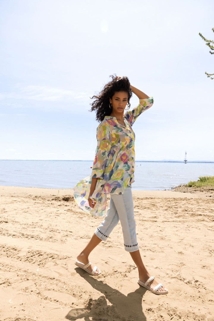 Modèle marchant sur la plage portant une blouse légère au motif artistique, coupe fluide et estivale.