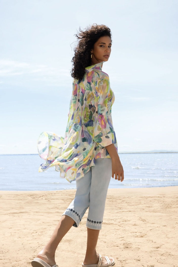 Femme portant une blouse légère au motif artistique sur la plage, créant un look estival et élégant.