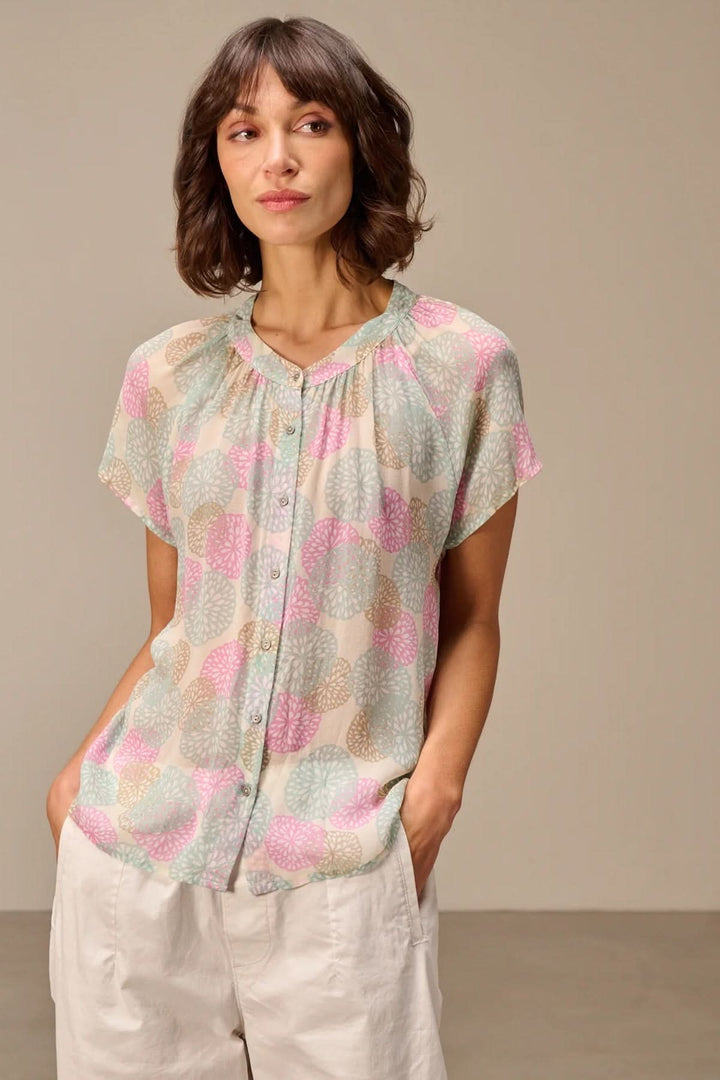 Blouse légère à manches courtes avec imprimé, fluide et féminine pour l'été, portée par une femme dans un cadre décontracté.