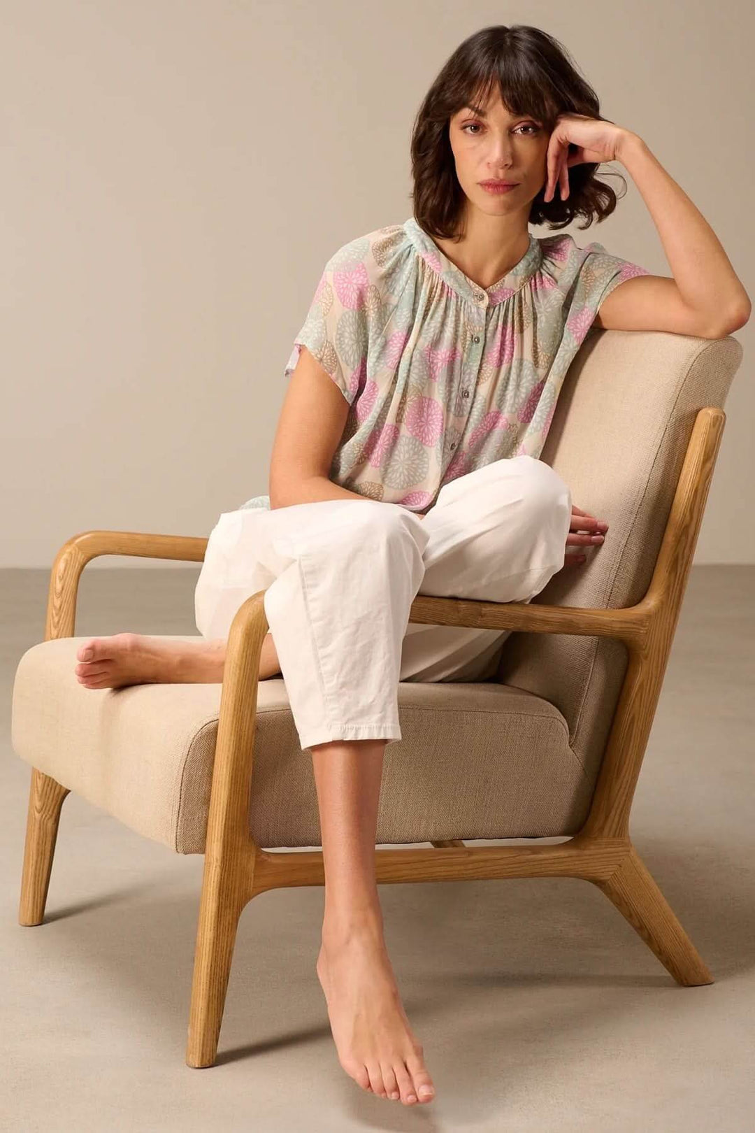 Femme portant une blouse légère à manches courtes avec imprimé, assise sur une chaise élégante, parfaite pour un style estival décontracté.