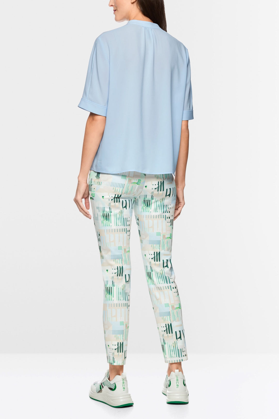 Femme portant une blouse à manches courtes bleue, vue de dos, avec un tombé élégant. Manches courtes, col montant, style moderne.