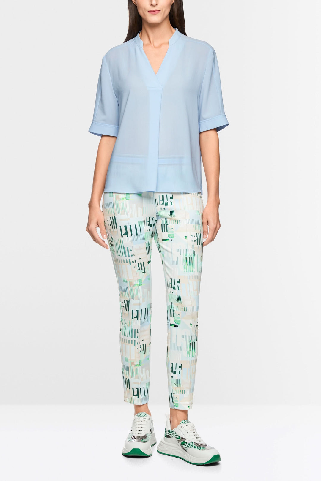 Blouse à manches courtes bleu clair avec encolure en V, manches revers, associée à un pantalon imprimé et des baskets blanches et vertes.