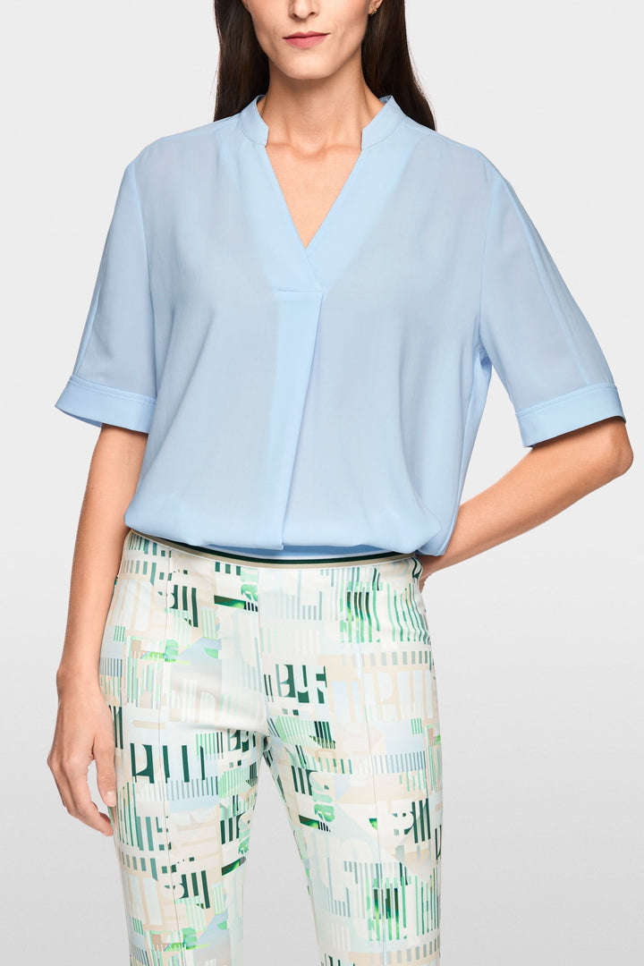 Blouse à manches courtes bleue avec encolure en V, coupe fluide et manches courtes à revers, parfaite pour un look minimaliste.