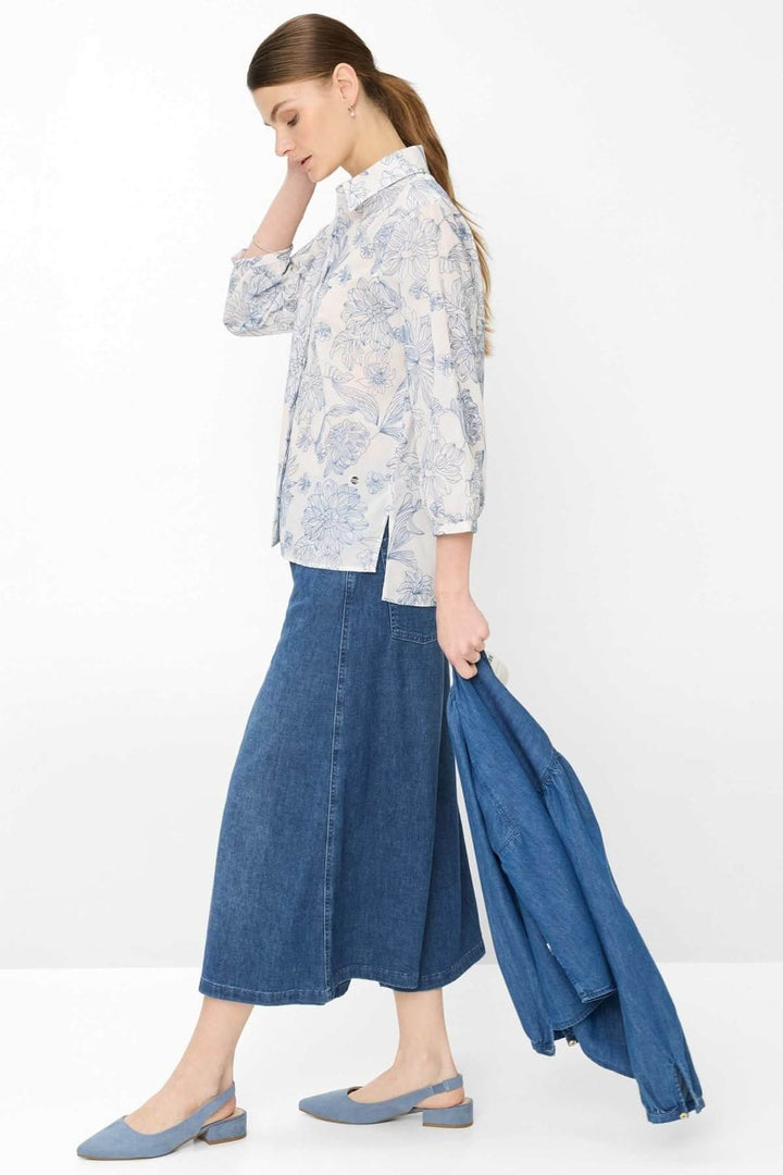 Femme portant la Blouse à motif floral VICKI avec jupe en jean et veste, présentant un style moderne et élégant.