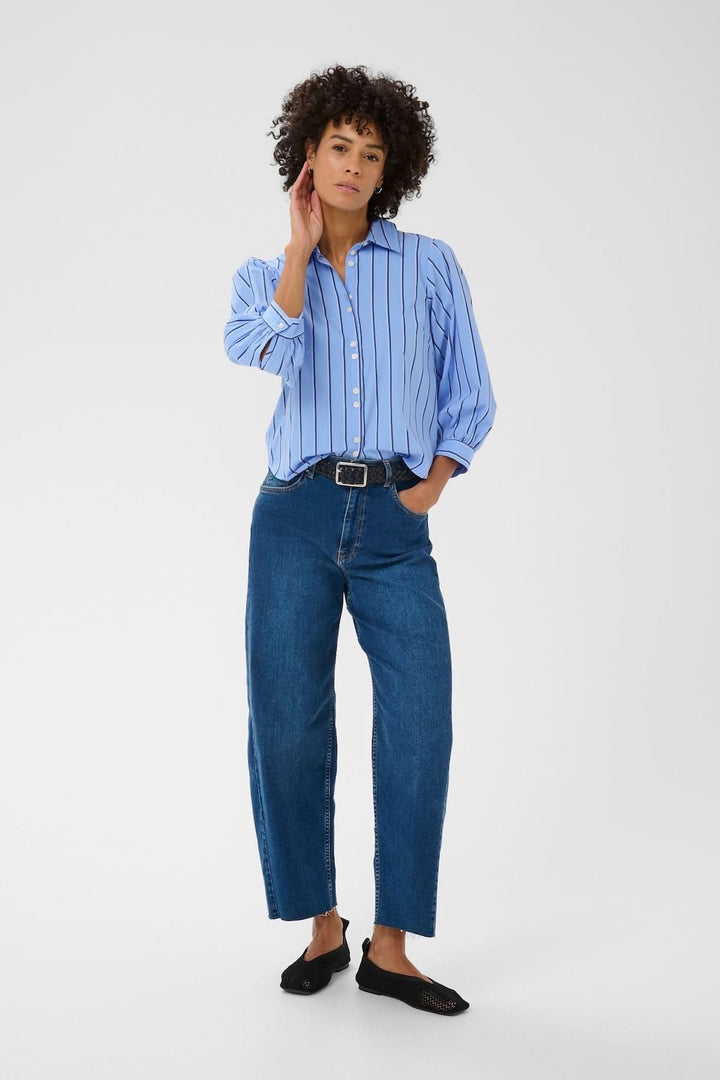 Femme portant la Blouse rayée Anais avec manches bouffantes, col structuré et jean décontracté.