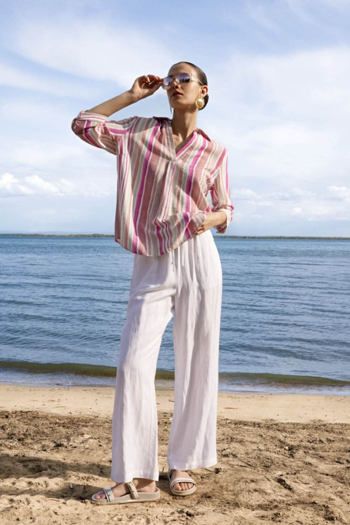 Femme portant une blouse rayée à encolure V sur une plage, manches trois-quarts, motif rayé vertical, look décontracté.