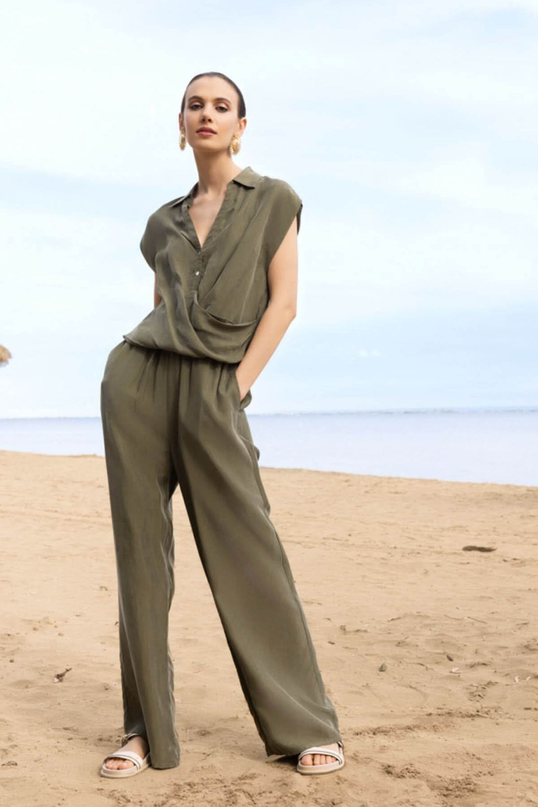 Femme portant une blouse sans manches à col chemise sur la plage, décontractée avec un style moderne et élégant.