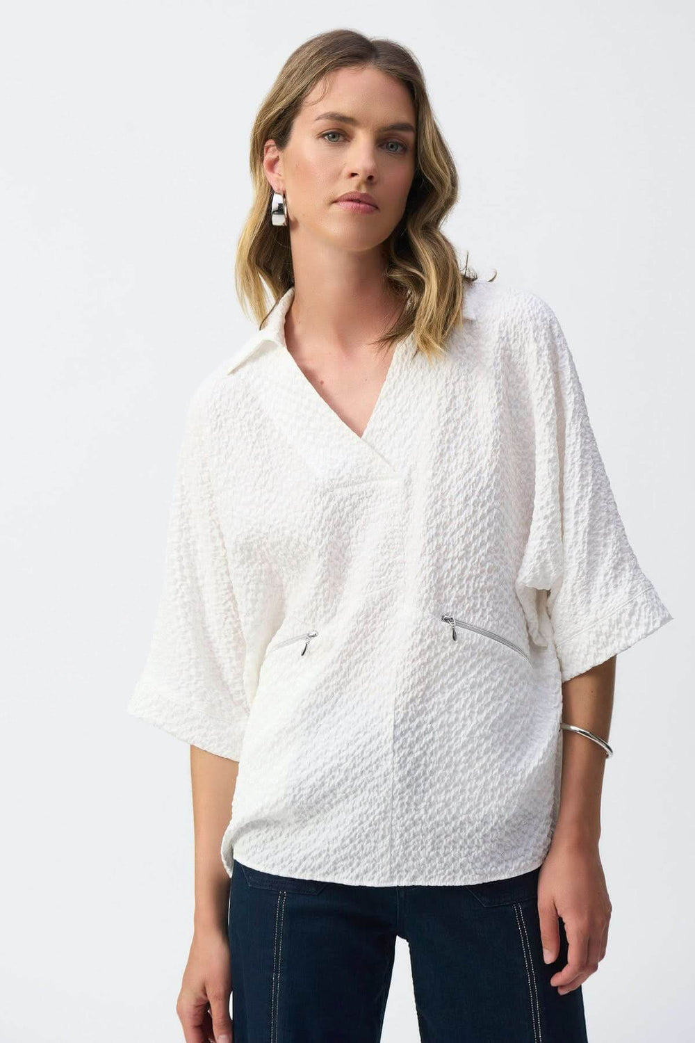Textured white blouse with V-neck, short sleeves, and zippered pockets, styled for a trendy yet casual look.