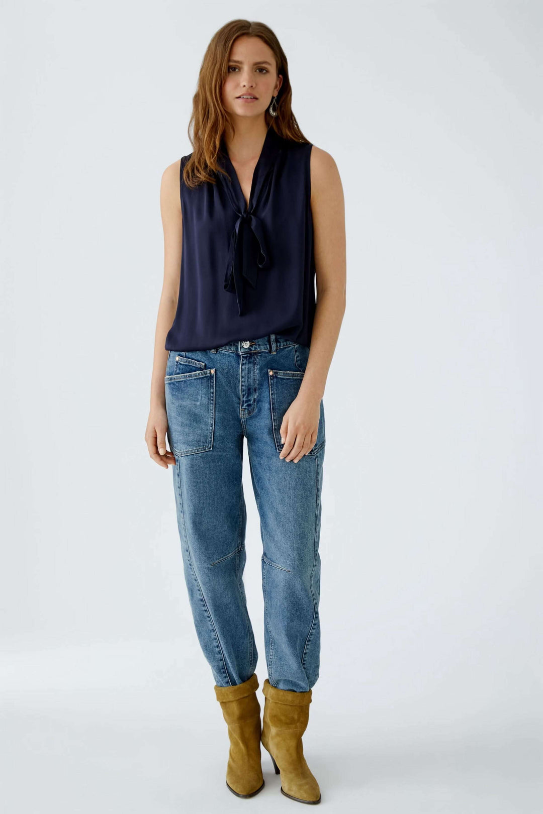 Femme portant une blouse évasée bleu marine avec un nœud et un jean décontracté, complétée par des bottes en daim.
