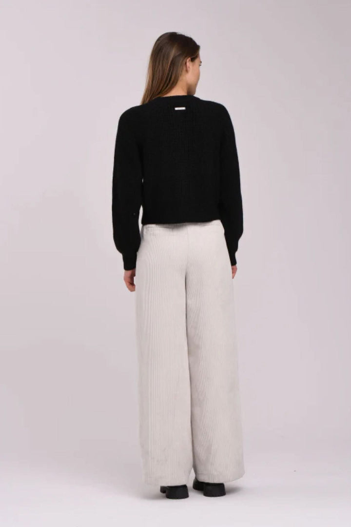 Femme de dos portant un cardigan noir élégant et un pantalon large en beige, montrant une tenue chic et confortable.