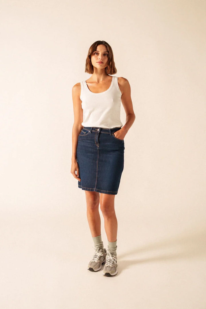 Femme portant la Camisole Bastia ajustée en blanc avec jupe en jean, mettant en valeur la silhouette pour un look quotidien élégant.