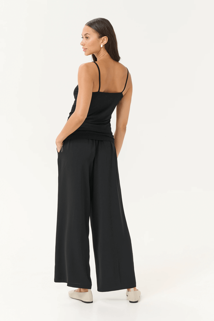 Femme portant une camisole Frida à bretelles réglables avec un pantalon noir fluide, vue de dos.