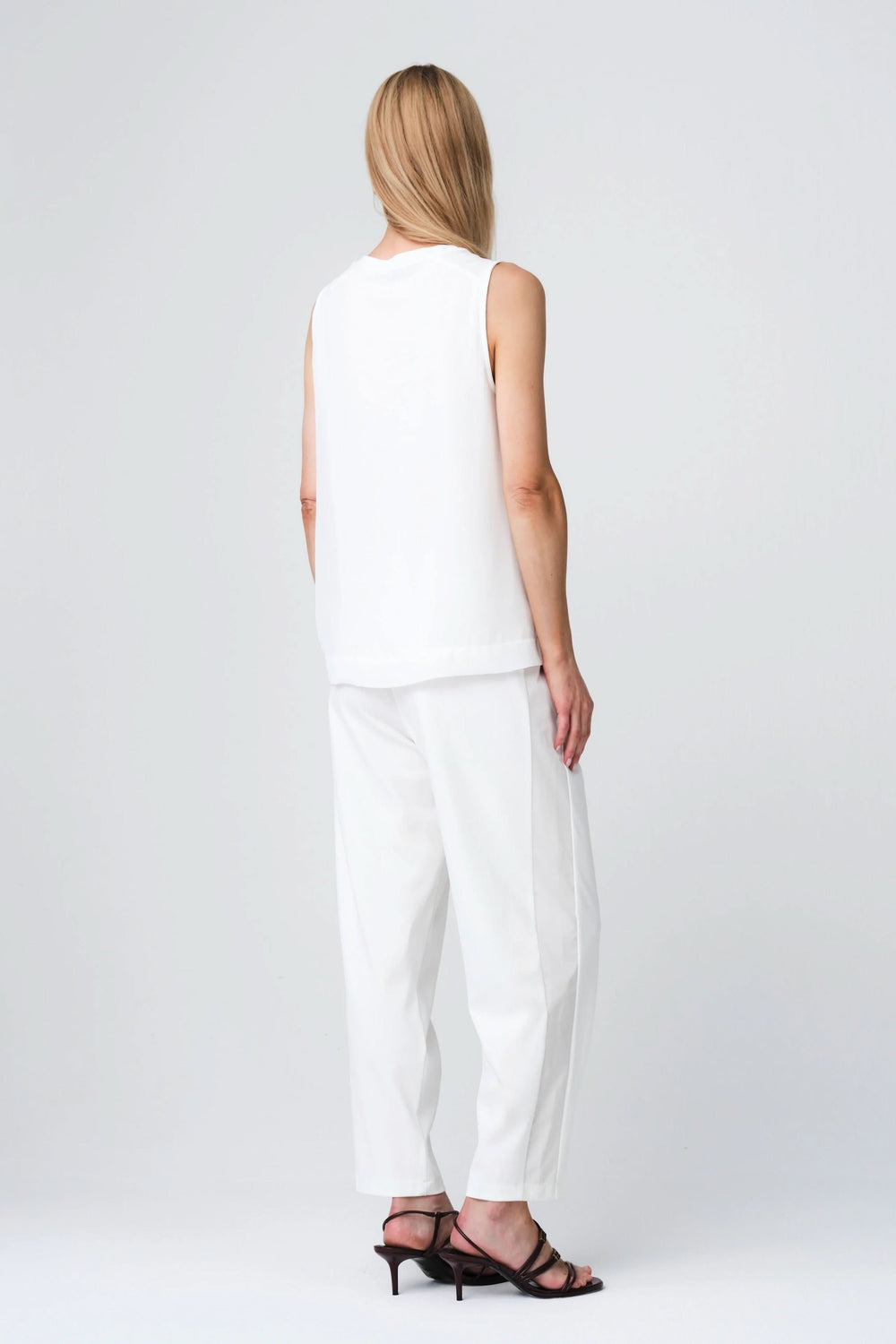 Dos de mannequin portant la Camisole Gini fluide sans manches, coupe droite en tissu blanc, assortie à un pantalon élégant et fluide.