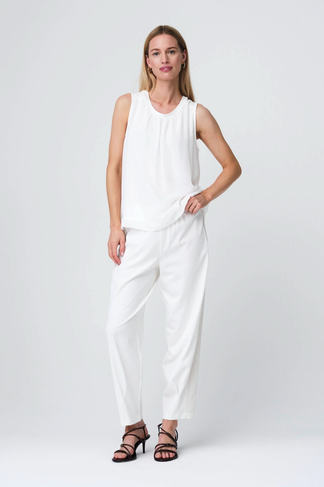 Femme portant la Camisole Gini fluide sans manches, en blanc, coupe légère et élégante, intégrée à une tenue chic et décontractée.