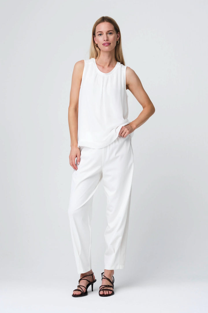 Femme portant la Camisole Gini fluide sans manches, en blanc, coupe légère et élégante, intégrée à une tenue chic et décontractée.