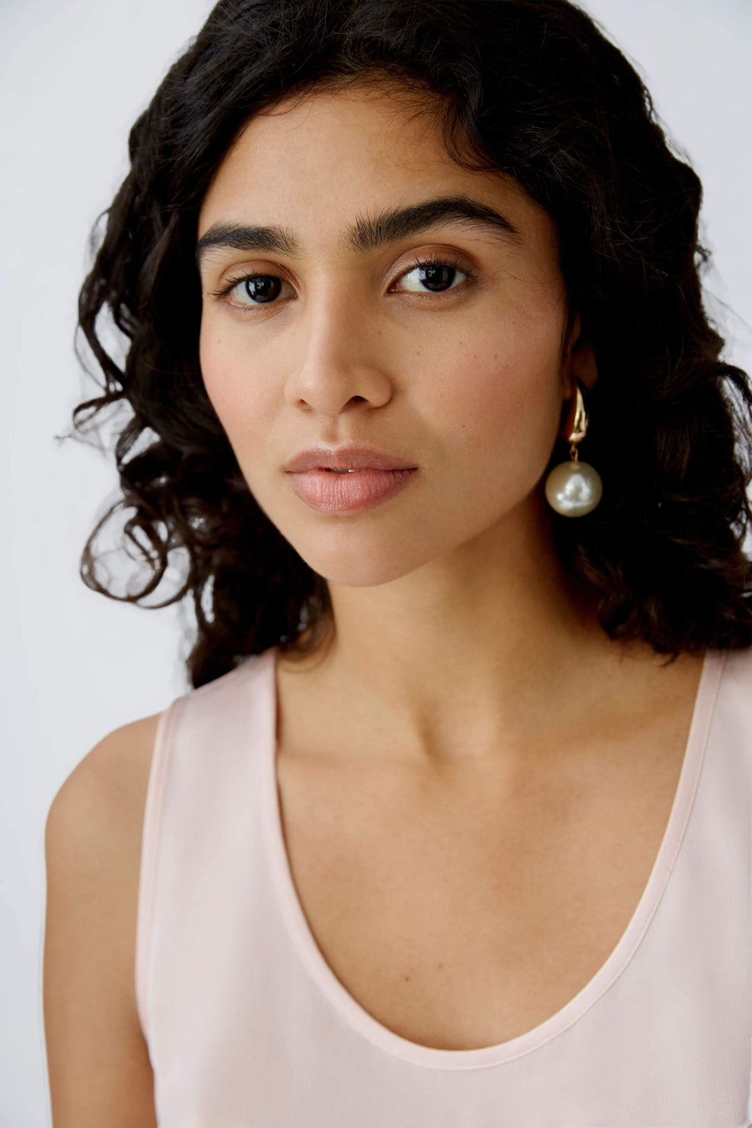 Femme avec des cheveux bouclés portant une camisole rose et des boucles d'oreilles en perles.