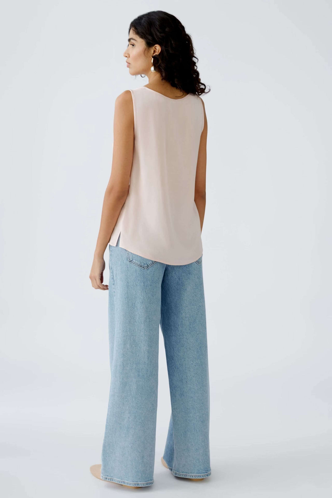 Femme portant une camisole beige derrière avec un style intemporel et un pantalon large en denim.