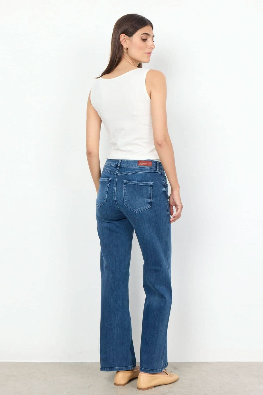 Femme portant une camisole basique blanche et un jean bleu, vue de dos, mise en valeur du style décontracté.