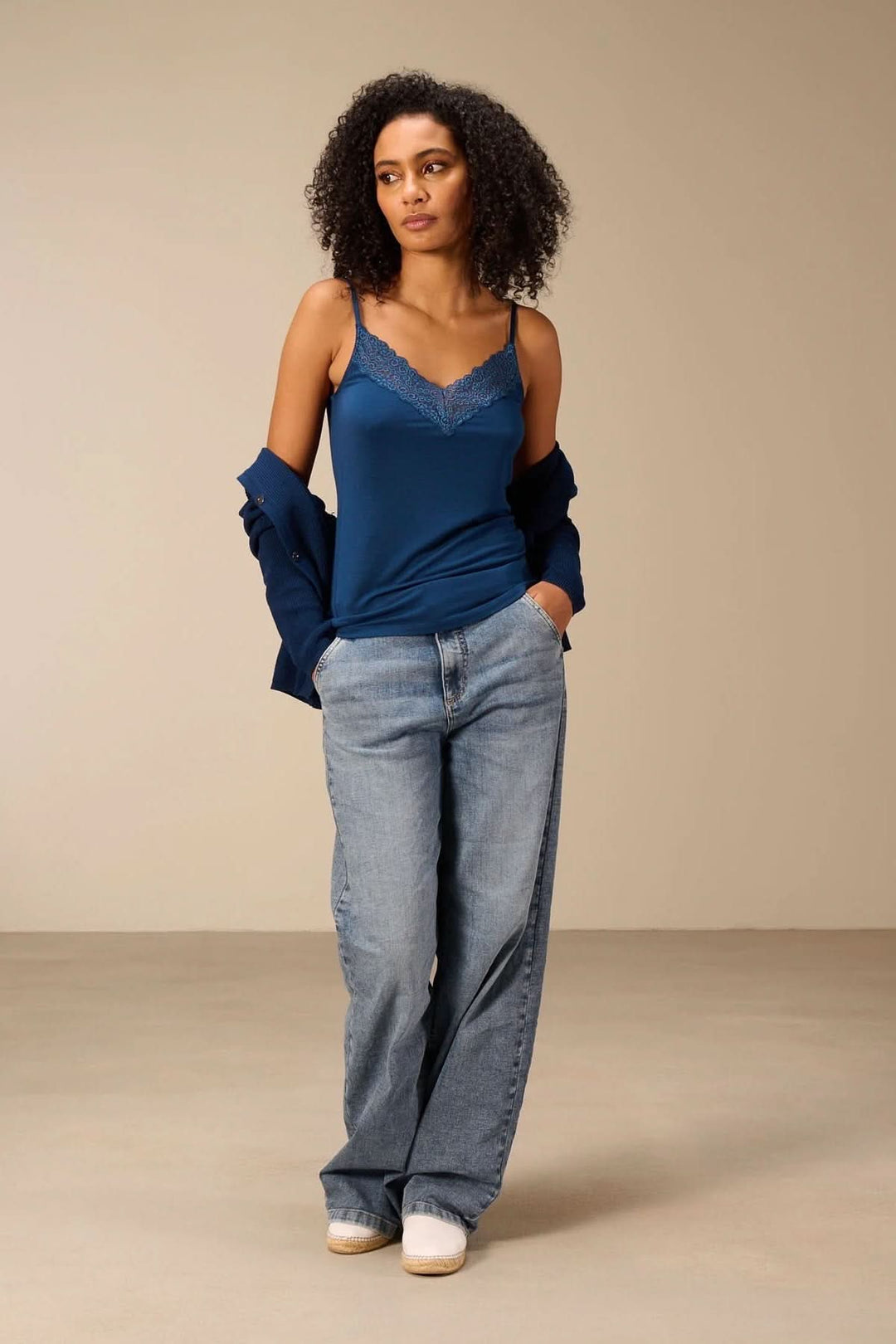 Femme portant une camisole à bretelles avec dentelle bleue, style décontracté avec jean et veste, mettant en valeur l'encolure en V.