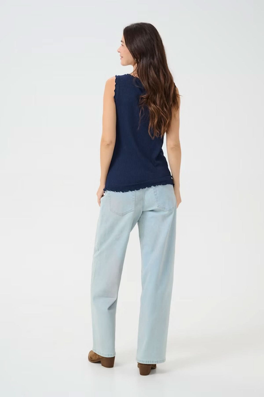 Femme portant une camisole à col froncé, vue de dos, associée à un pantalon clair pour un look estival décontracté.