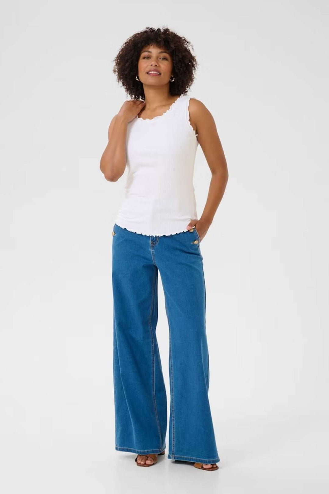 Camisole blanche à col froncé, portée avec un pantalon en denim large, parfaite pour un look estival décontracté.