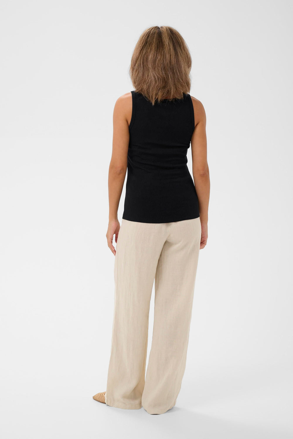 Femme portant la camisole côtelée Ribba avec détail anneau, vue de dos, en noir, agencée avec un pantalon beige.