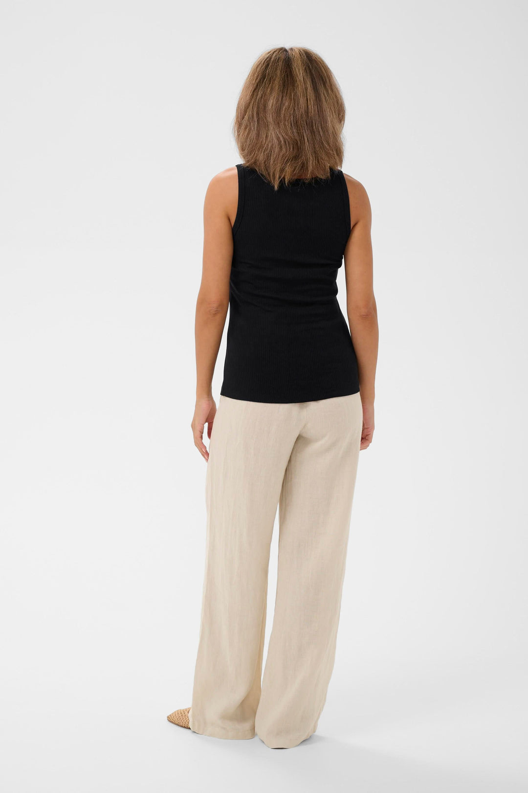 Femme portant la camisole côtelée Ribba avec détail anneau, vue de dos, en noir, agencée avec un pantalon beige.
