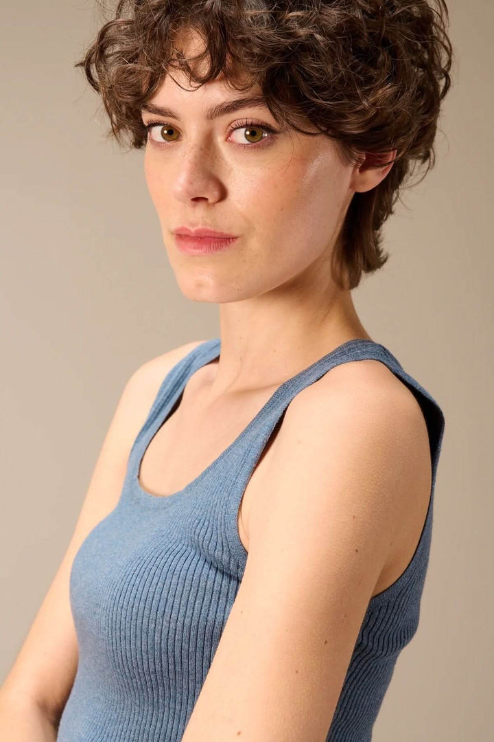 Femme portant une camisole côtelée ajustée col rond, avec bretelles larges et texture côtelée, offrant une coupe minimaliste et confortable.