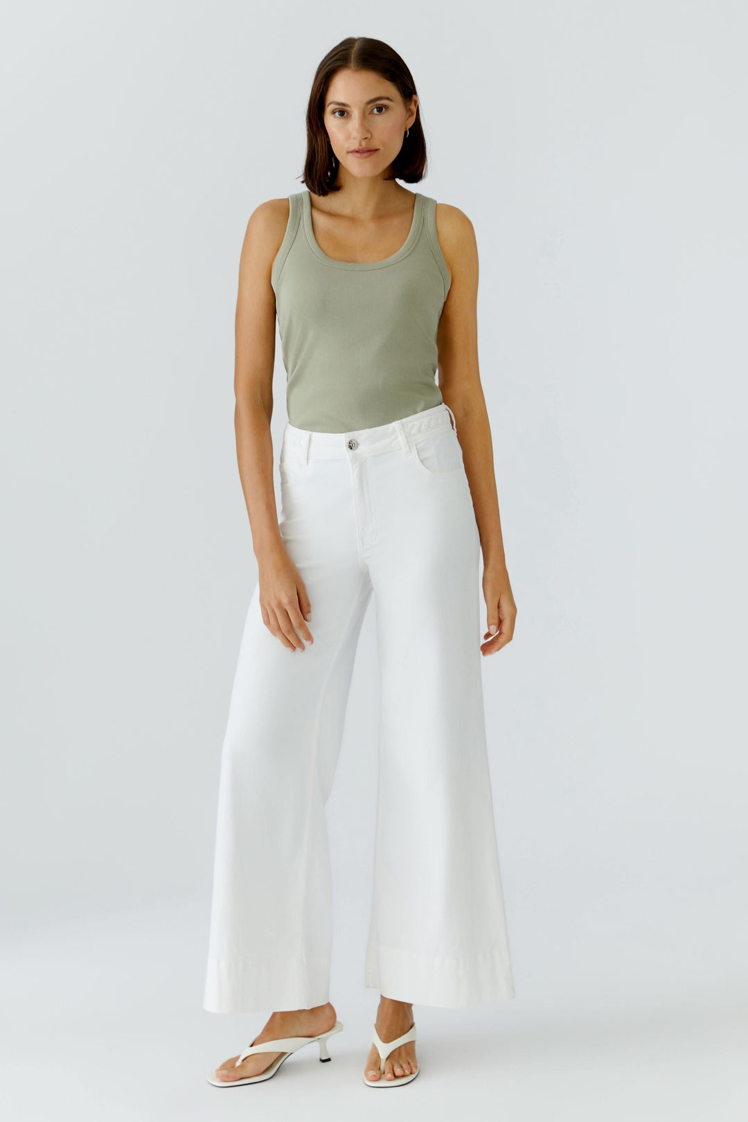 Femme portant une camisole côtelée essentielle verte avec un pantalon large blanc, look décontracté et élégant.