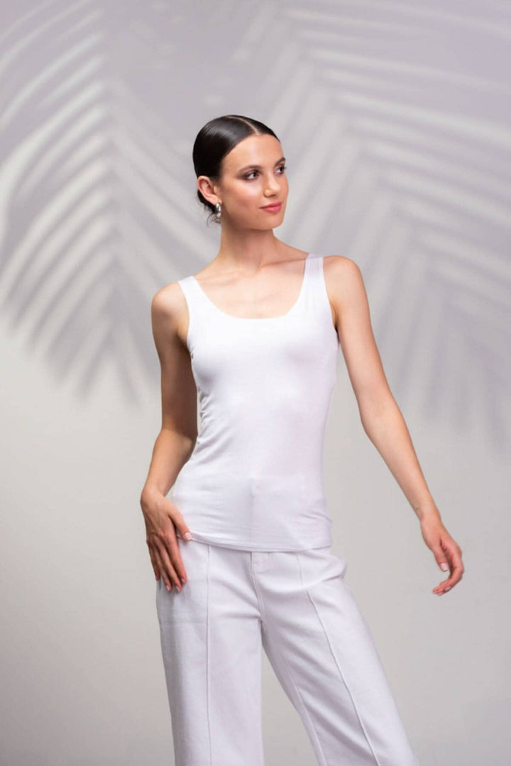 Camisole blanche à encolure carrée portée avec un pantalon blanc, présentée sur fond tropical.