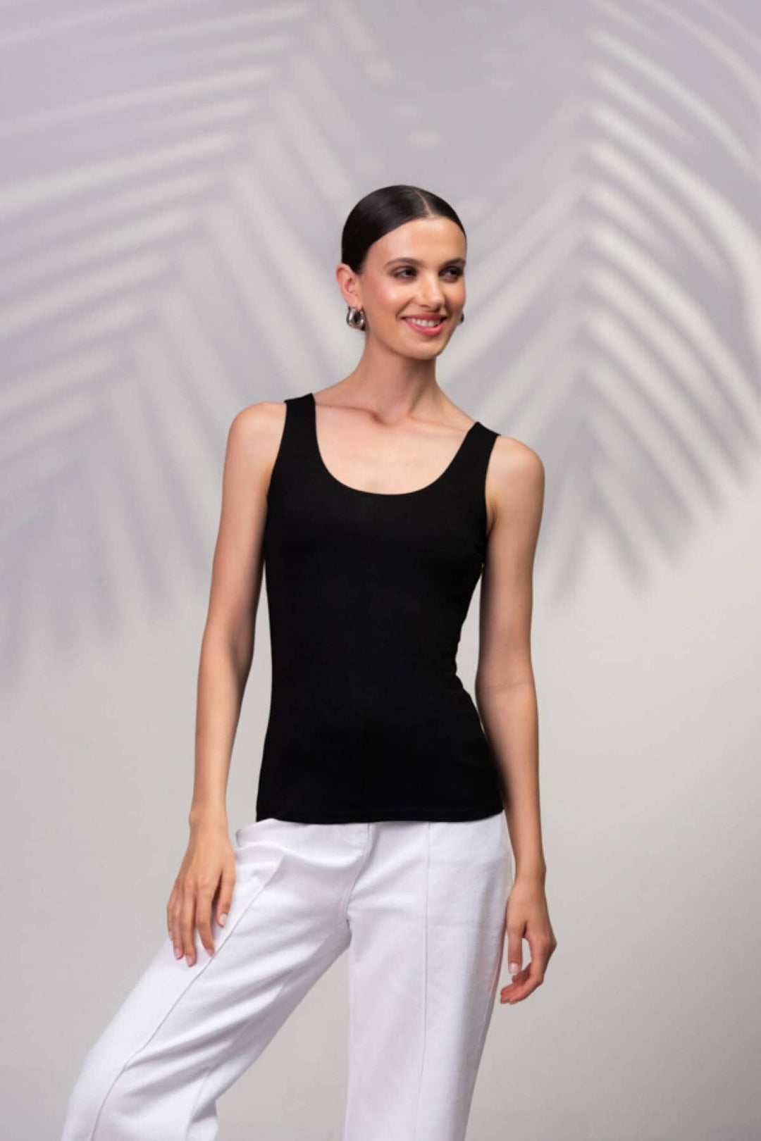 Modèle portant une camisole noire à encolure carrée avec bretelles larges et pantalon blanc.