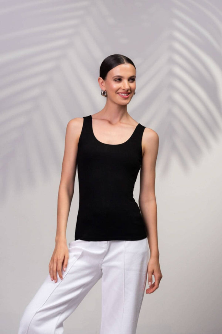 Modèle portant une camisole noire à encolure carrée avec bretelles larges et pantalon blanc.
