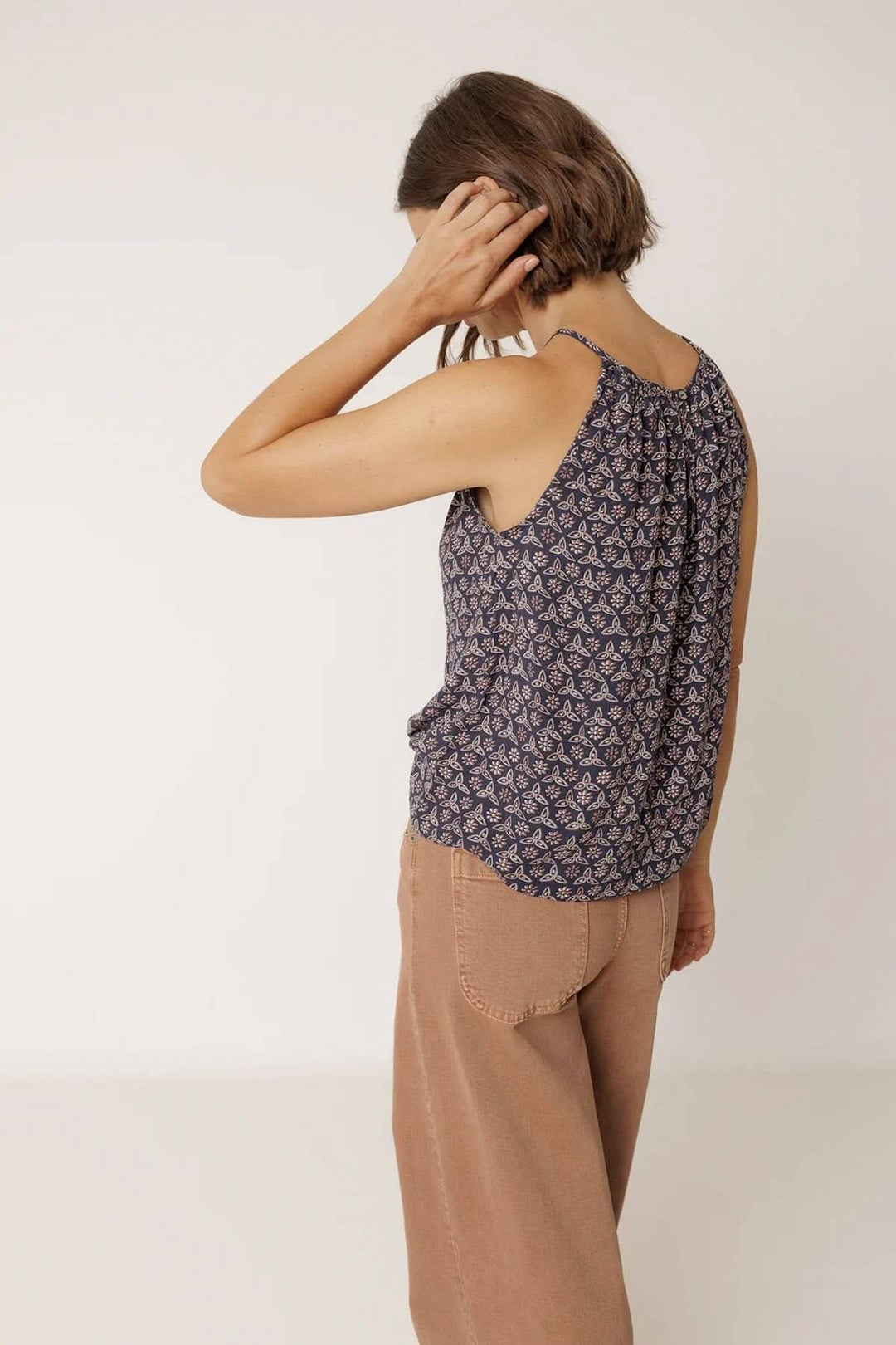 Femme portant une camisole fluide à encolure froncée, sans manches, avec un motif élégant, vue de dos.