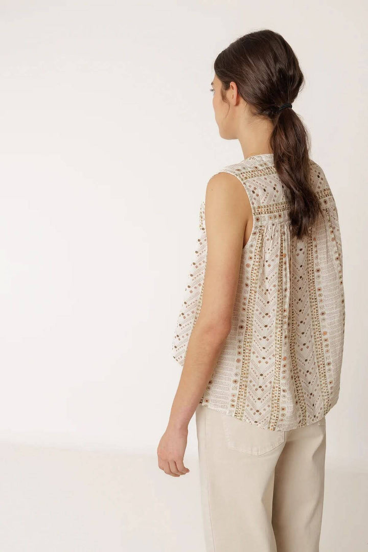 Femme portant une camisole fluide imprimée sans manches, style léger et élégant, en toile de fond neutre.