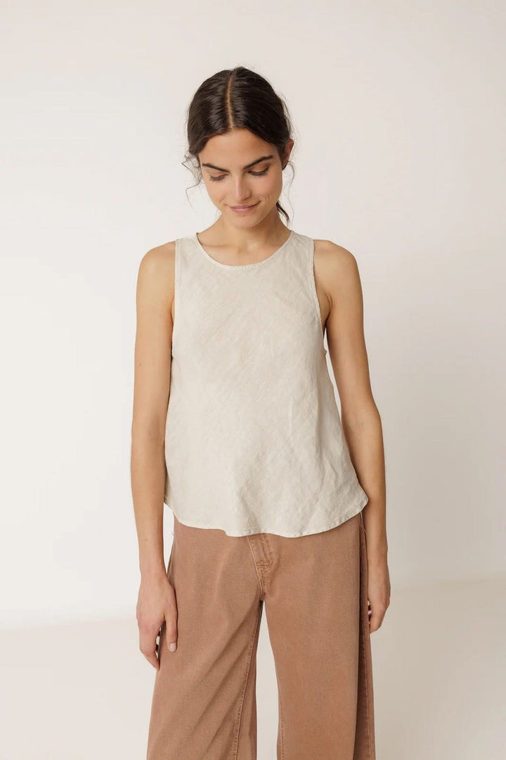 Femme portant une camisole fluide sans manches à encolure ronde, tissu léger et respirant, coupe légèrement évasée, couleur neutre.