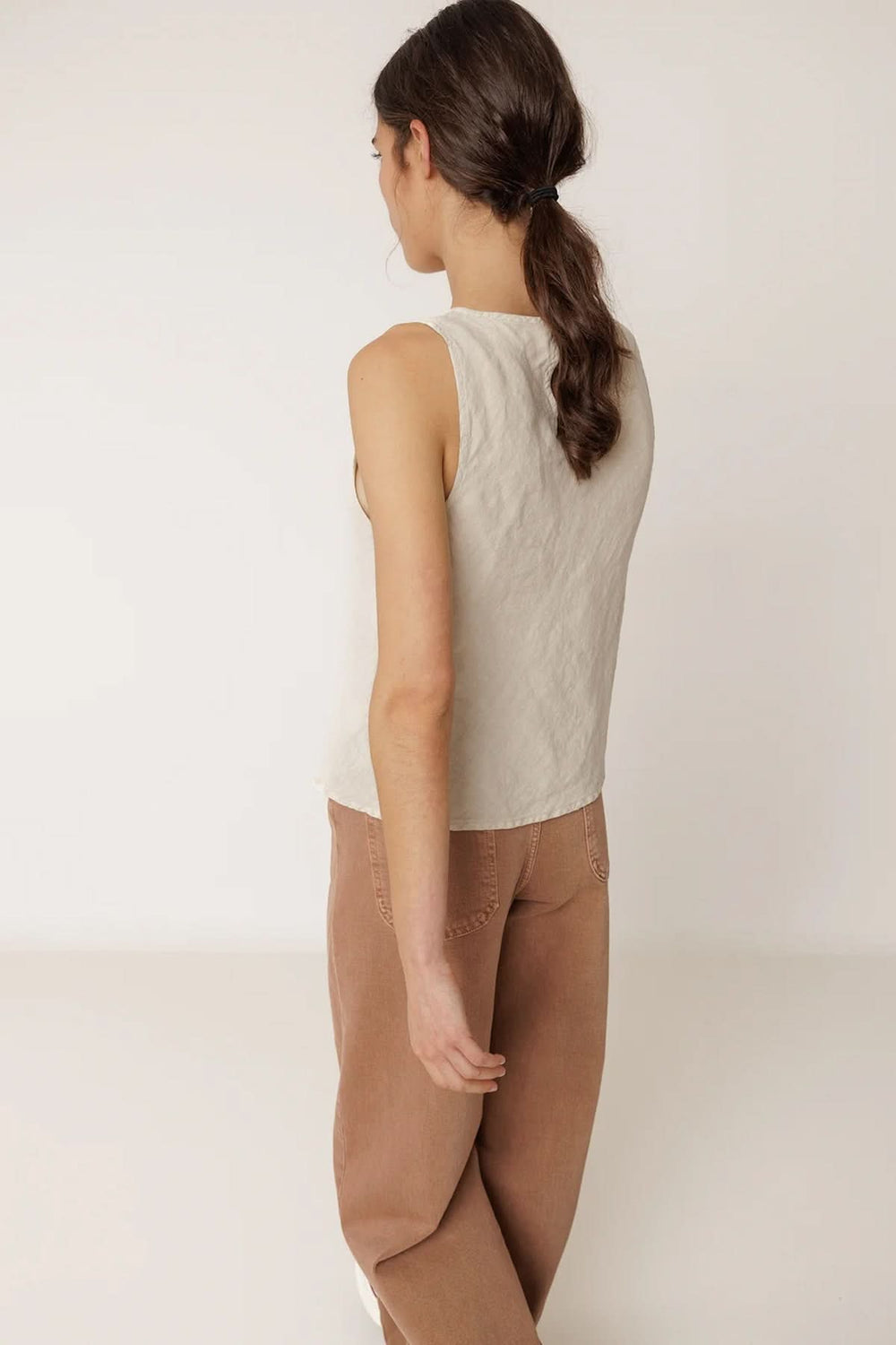 Dos d'une femme portant une camisole fluide sans manches à encolure ronde, tissu léger et respirant, coupe légèrement évasée.